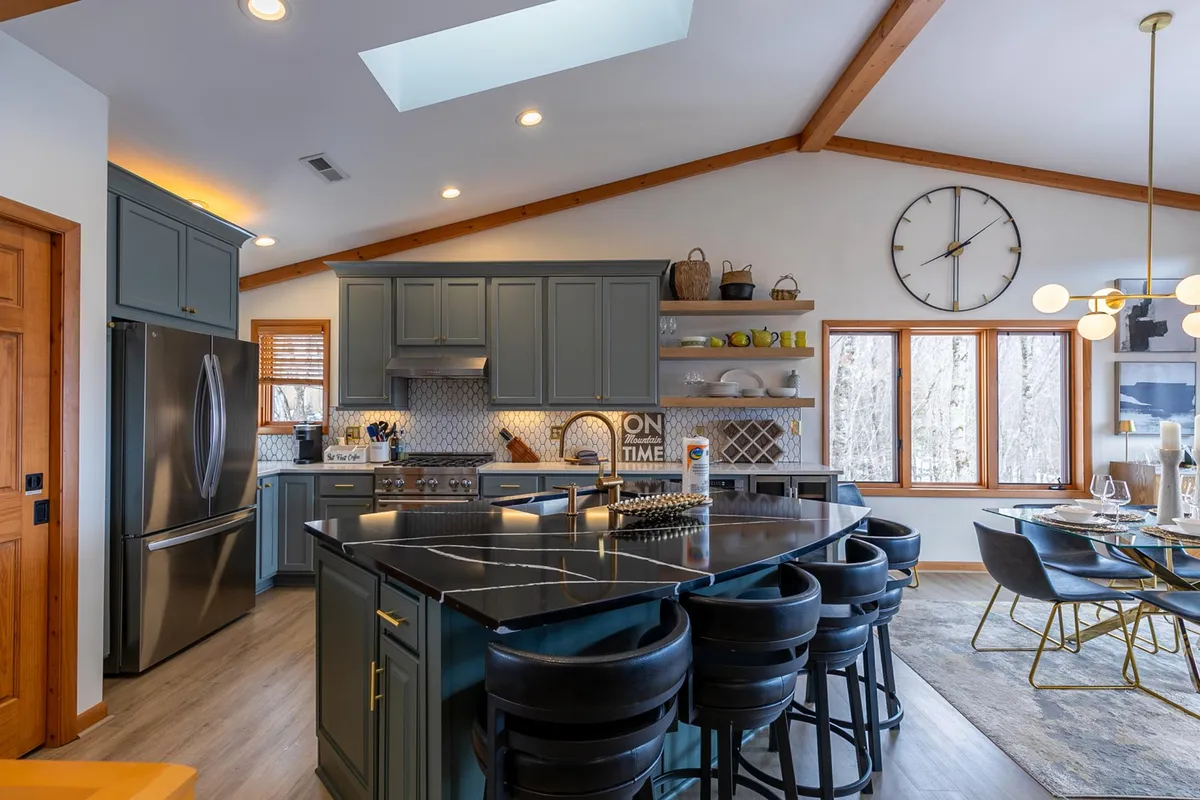 A warm and spacious kitchen and dining area, highlighted by a large granite island, elegant cabinetry, modern dining table for six, and abundant natural light from the windows. The space is designed for meals, entertaining, and morning routines.