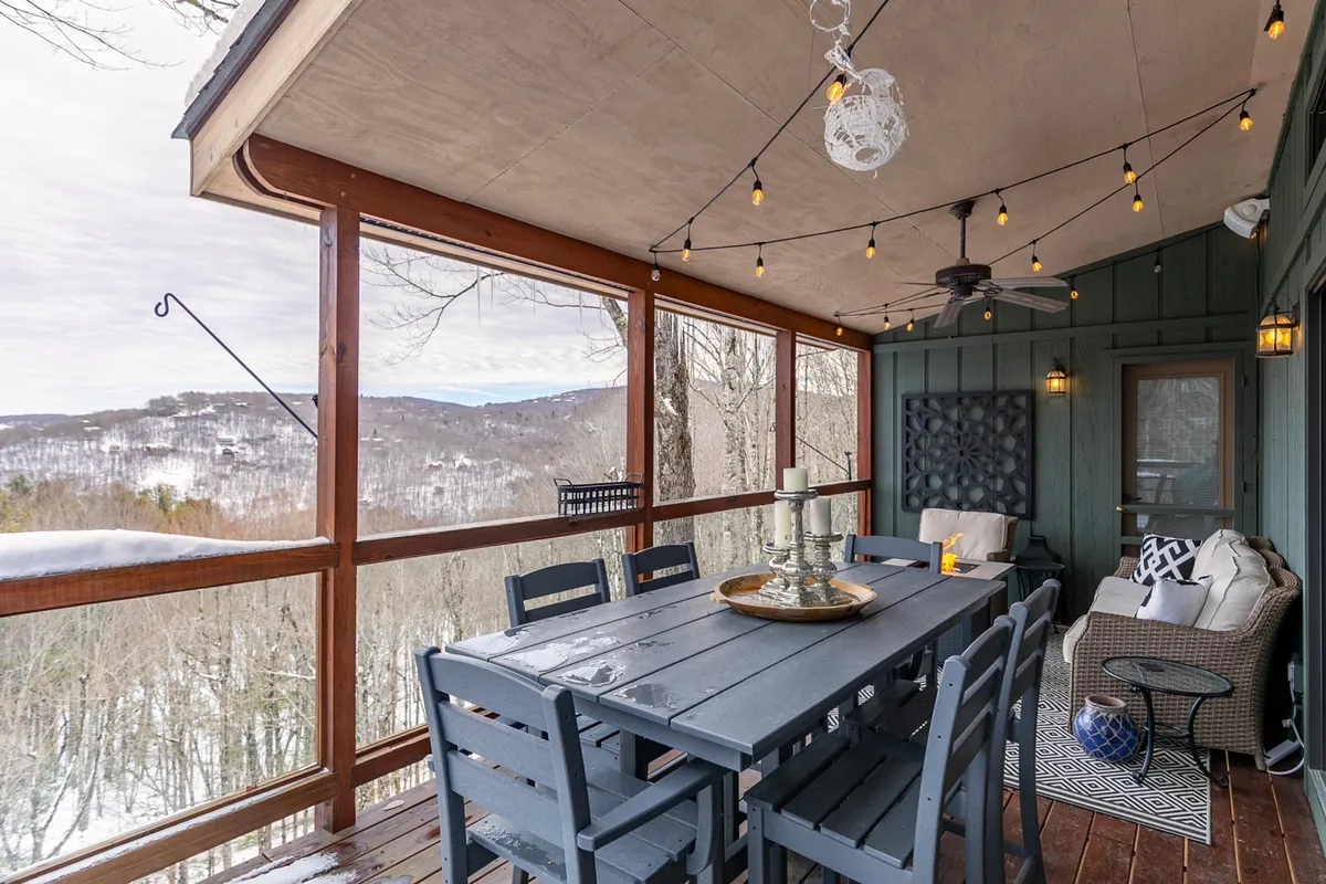 An inviting outdoor dining area with a table, decorative chair, hanging lights, and a scenic view of snow-draped mountains. The cozy setup hints at après-ski moments and gatherings with friends or family, all set against the backdrop of the wintry landscape.