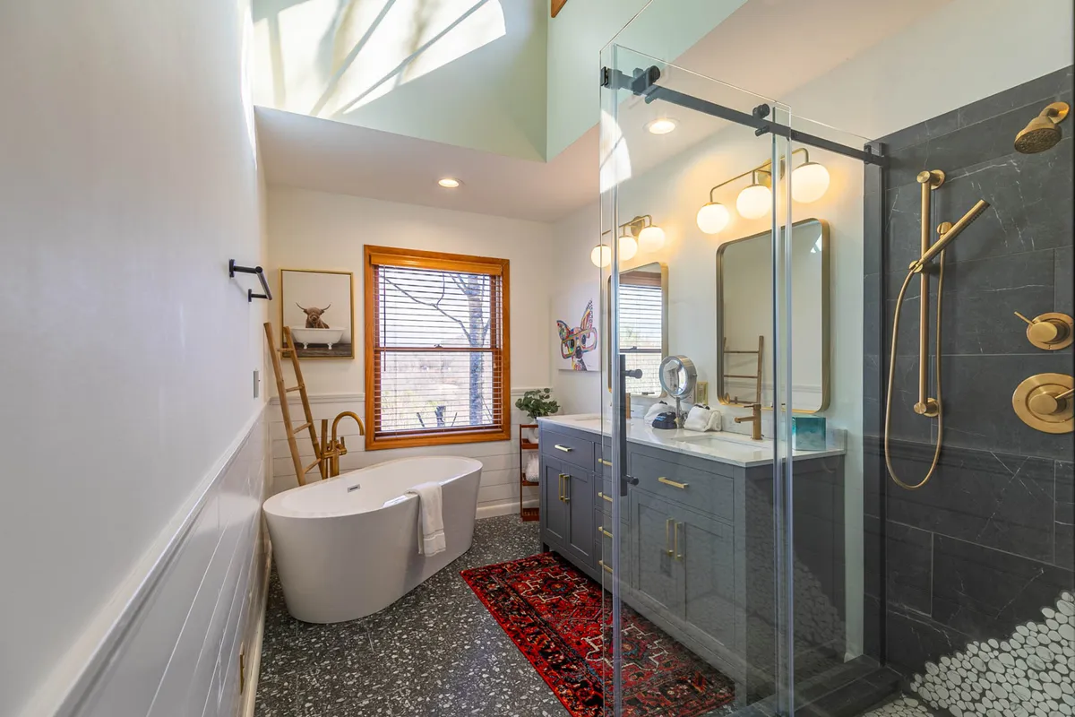 A modern, spa-inspired bathroom featuring a freestanding bathtub, spacious glass shower enclosure, dual-sink vanity, and a large window that brings in natural light. The ambiance is calm and rejuvenating, perfect for a luxurious soak or refreshing shower.
