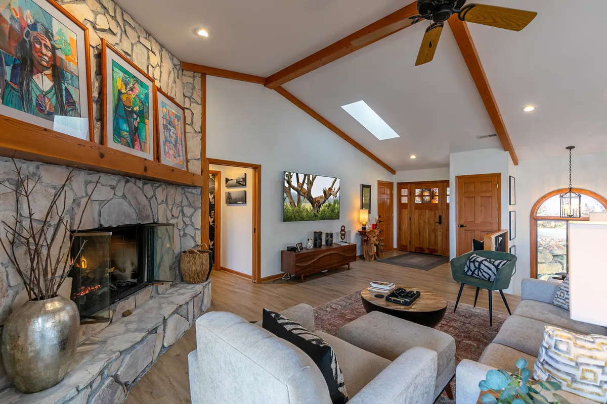 A cozy living area with a stone fireplace, colorful artwork, and comfortable sofas arranged around the fire. The space exudes warmth and is ideal for relaxing with family or friends after a day on the slopes.