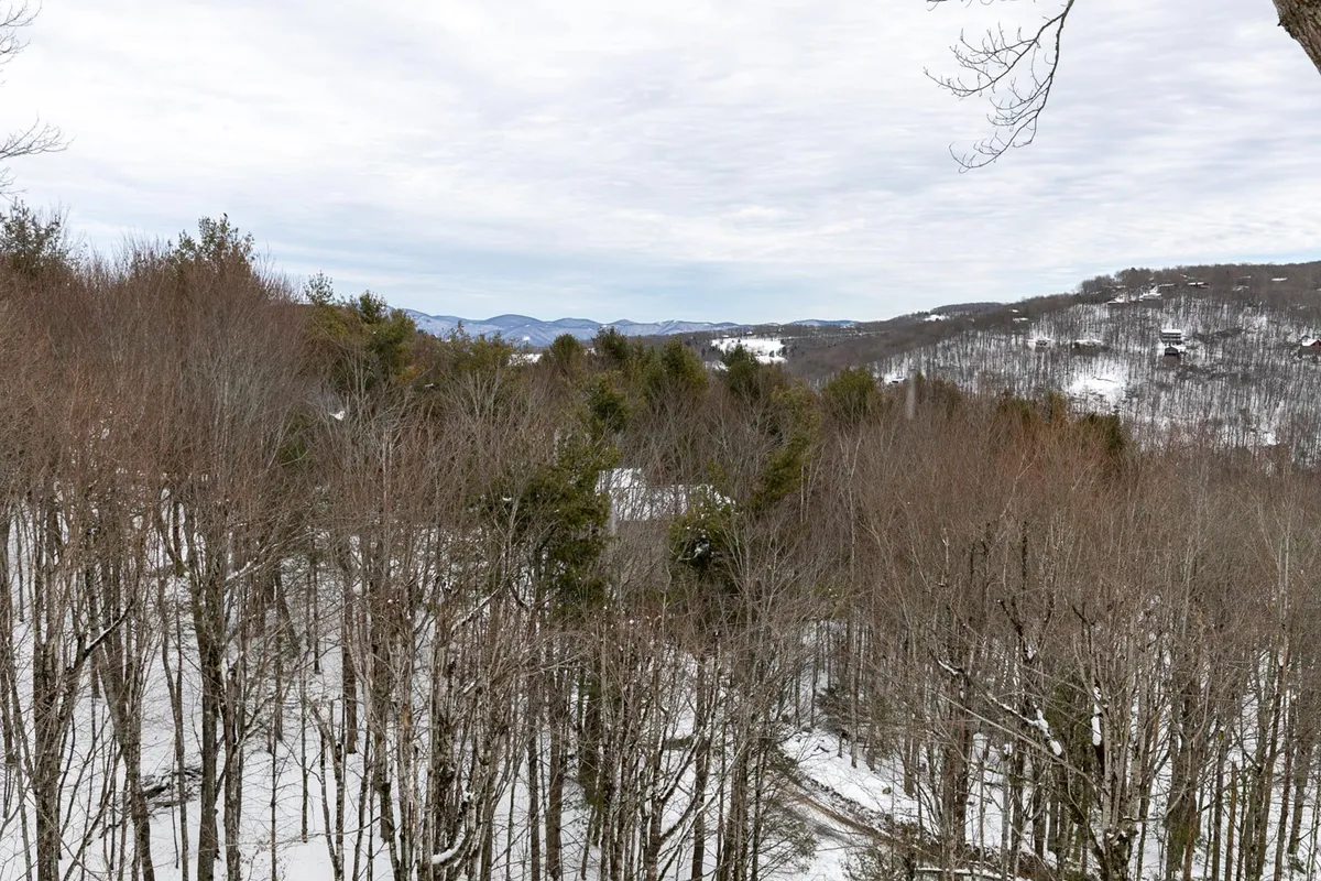 A serene landscape featuring snow-covered trees, distant mountain vistas, and a cloudy winter sky. The scene captures the crisp, fresh beauty of Beech Mountain during the winter months, suggesting an ideal environment for skiing and other winter adventures.