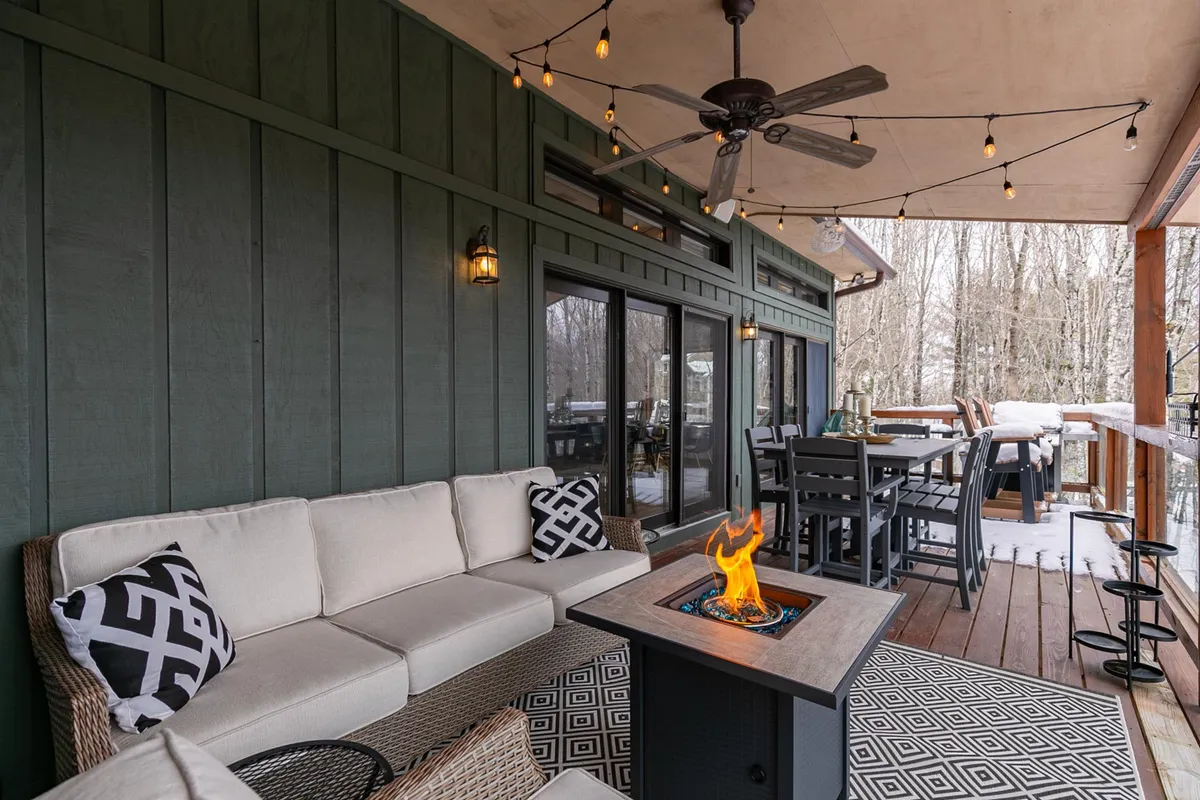 A warm and welcoming outdoor seating area with a fire pit, decorative pillows, and comfortable chairs arranged on a wooden deck. The setting overlooks nature, making it ideal for relaxing evenings or intimate conversations under the stars.