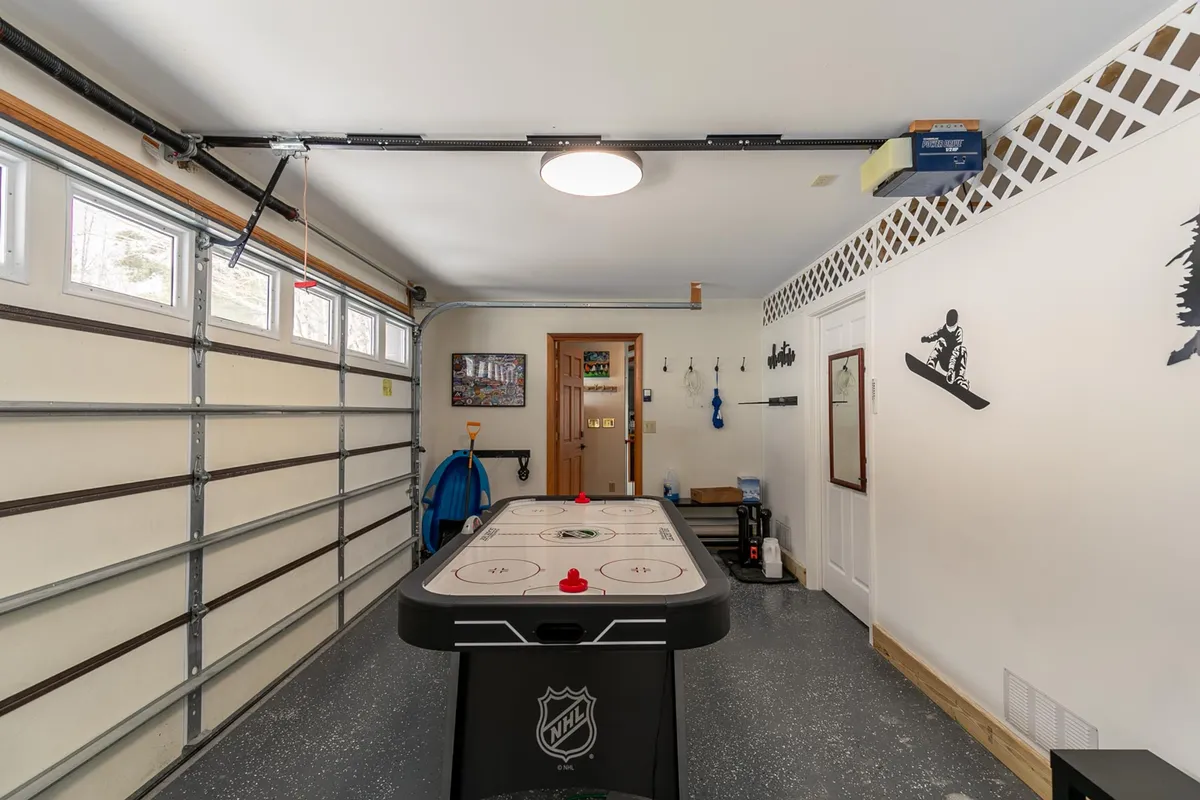 A multi-purpose gear storage area featuring an air hockey table, garage door access, and visible sporting equipment storage. The decor features sports-themed wall decorations, evoking both fun and practicality.