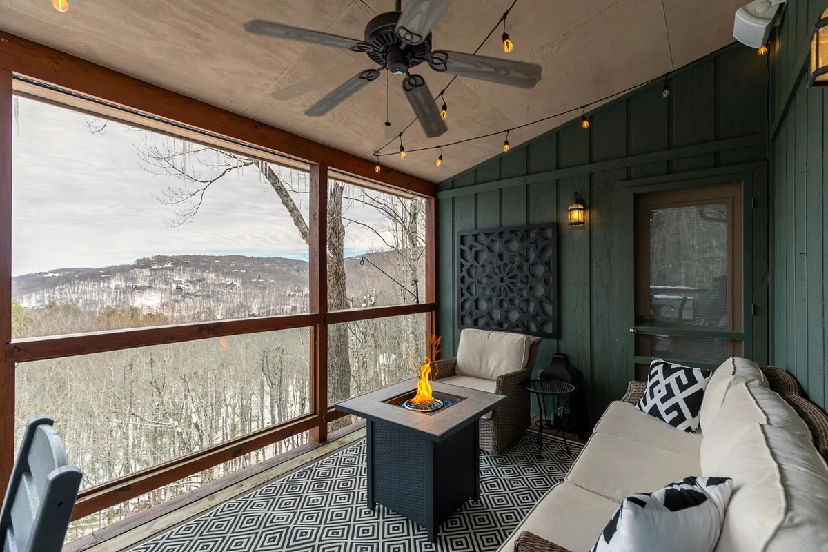 An inviting fire pit area is framed by comfortable seating and scenic mountain views, with a decorative wall panel adding a cozy touch. The space is ideal for gathering, socializing, or relaxing after a day of indoor or outdoor fun, seamlessly blending the comforts of home with the adventure of the outdoors.