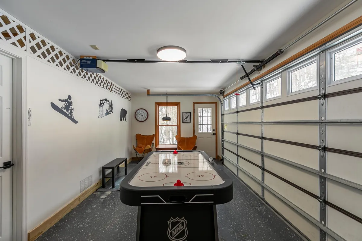 A bright, energetic garage game area outfitted with an air hockey table and a relaxed seating spot. Decorative wall art adds to the playful vibe, inviting guests of all ages to gather and compete.