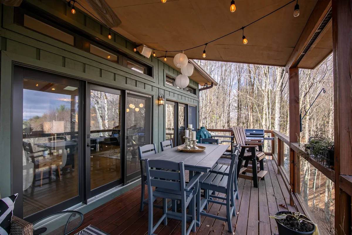 An inviting outdoor dining area on a deck, featuring a table set under hanging string lights with a beautiful natural backdrop of trees. The space radiates a cozy atmosphere, ideal for couples to enjoy breakfast or a romantic meal surrounded by the serenity of nature.