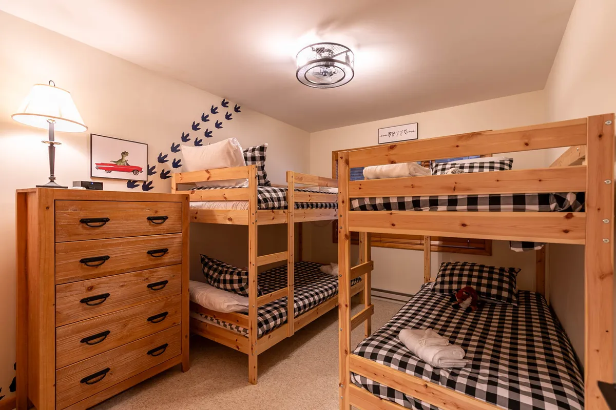 A cheerful bunkroom with twin-over-twin beds, a dresser, lamp, and playful wall decor. The space feels inviting and functional, designed for children or friends to share stories and create memories together.